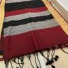 Black and red striped cotton saree with tassel details displayed on a woven mat.