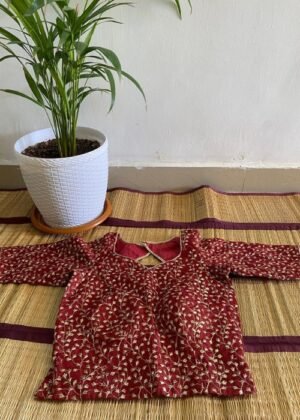 Stunning red embroidered blouse with golden floral patterns on a woven mat.